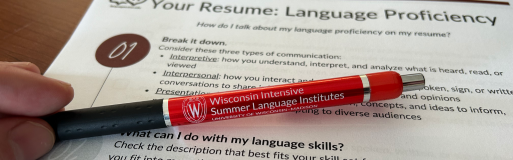 A hand holds a red pen labeled "Wisconsin Intensive Summer Language Institutes." It rests on a document about resume language proficiency and skills.
