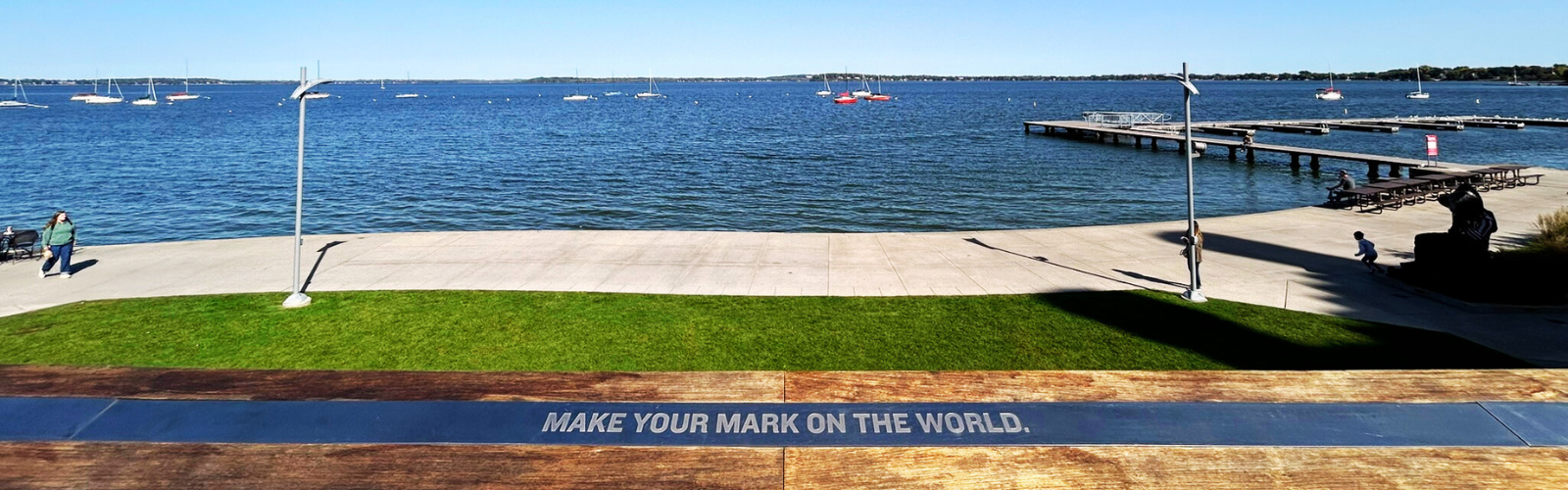 A plaque that states "make your mark on the world" next to a lake
