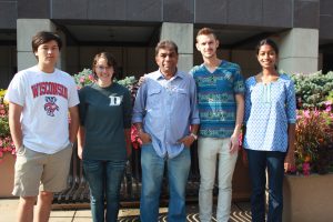Five people stand outside next to each other, smiling at the camera