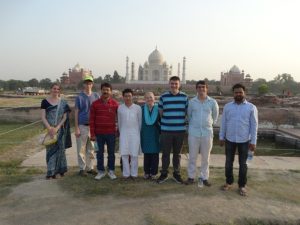 A group of seven people stand smiling in front of the Taj Mahal.