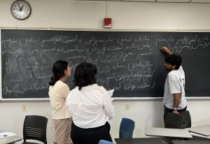 One person writes script on a chalkboard while two people watch. 