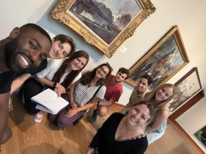 Eight people stand in an art gallery and smile at the camera