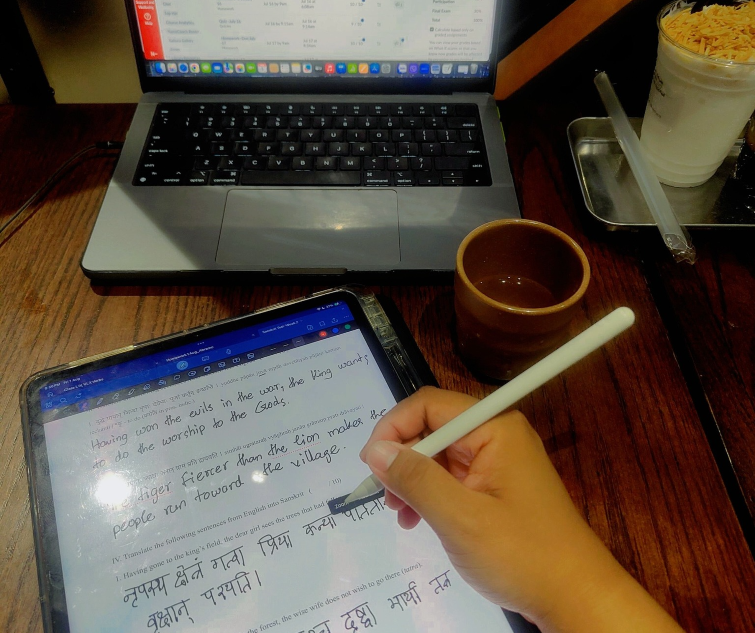 A person uses a stylus on a tablet displaying handwritten notes. A laptop with a red screen is open in the background.