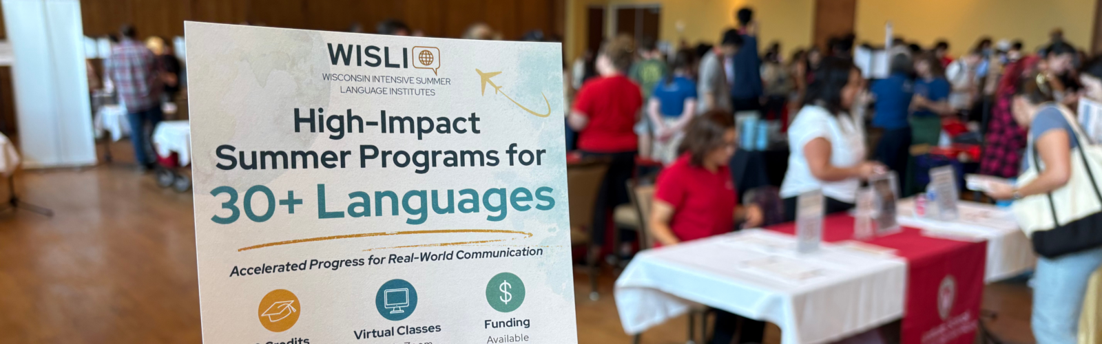 WISLI promotional sign advertising high-impact summer programs in 30+ languages at a campus resource fair.