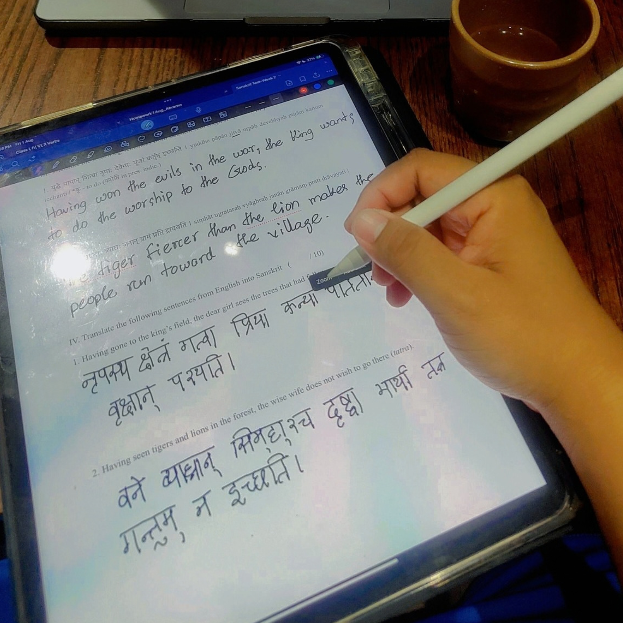 A student uses a stylus to complete a Sanskrit language exercise on a tablet at a café table, with a laptop showing course grades and drinks nearby.